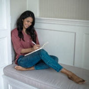 A woman sitting on a sofa and leaning against a wall writing on a notebook on her lap